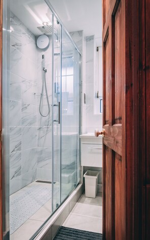 A modern bathroom with a glass-enclosed shower, marble tiles, a wooden door, and a white sink. - Hotel Quality Stay 2 Bed Apt near the City Centre (London)