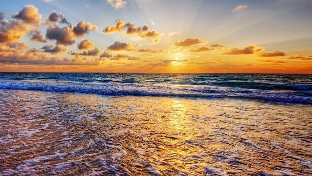 A beach with waves and a sunset.