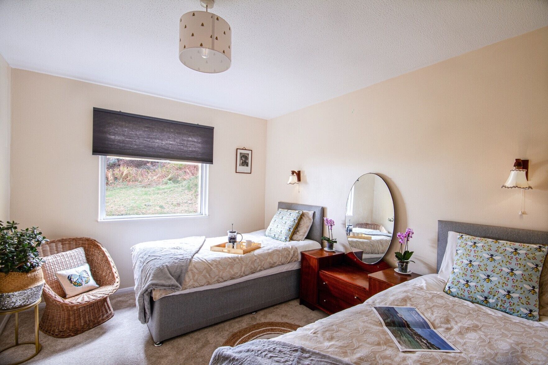 Une chambre avec deux lits, une fenêtre donnant sur un beau paysage, une chaise en osier, une table de chevet et un miroir.