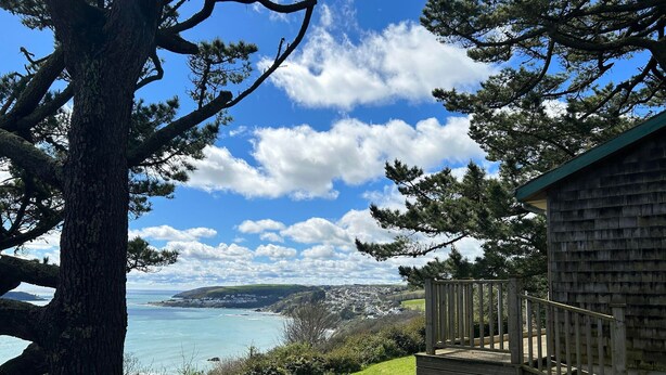 A coastal view with a large tree, a wooden deck, and a building with a sloped roof. - Windwhistle - Two Bedroom Cottage, Sleeps 4 (Saint Martin-by-Looe)