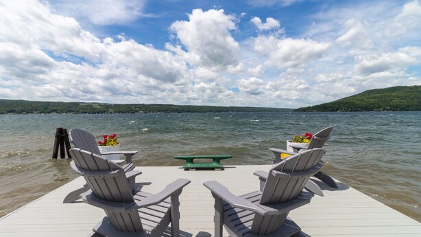 A deck with Adirondack chairs and a picnic table overlooking a lake with a view of a distant shoreline.
