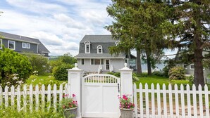 A two-story house with a white picket fence, a covered porch, and a view of a lake.