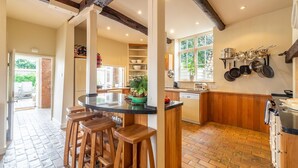 Una cocina con una isla central, taburetes de madera, suelo de ladrillo y un colgador para ollas.