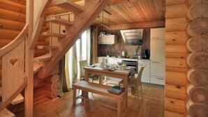 Interior de una cabaña de madera con escalera espiral, zona de comedor y cocina.