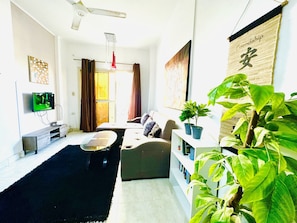 Relax in this inviting living room with a flat-screen TV, comfortable sofa, and a large potted plant.