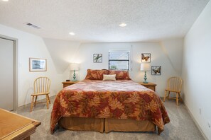 A bedroom with a large bed, two chairs, a nightstand, a window with blinds, and wall art. - Beachfront Home with Beautiful Views (Galveston)