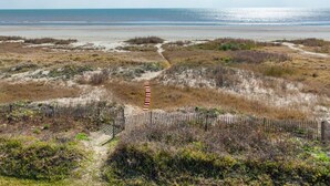 Ein Küstenpfad führt zum Strand, begleitet von einem Holzzaun und vereinzelter Vegetation.