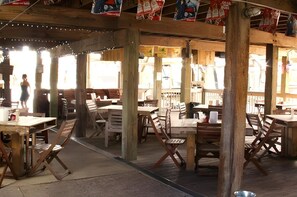 An outdoor wooden dining area with tables and chairs, supported by wooden beams and columns. - Beachfront Home with Beautiful Views (Galveston)