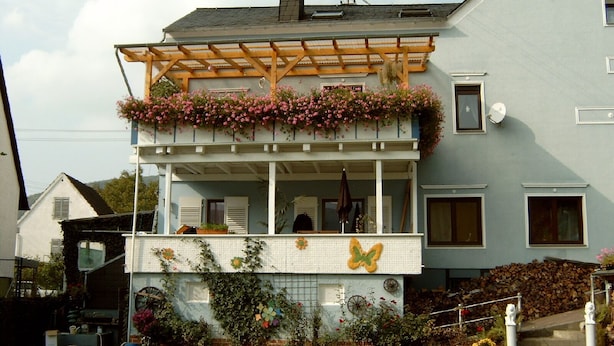 A two-story house with a balcony covered by a wooden pergola, adorned with pink flowers.