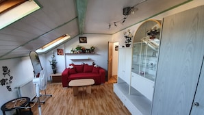 A cozy living room with a red sofa, wooden flooring, a white cabinet with glass doors, and a ceiling fan.