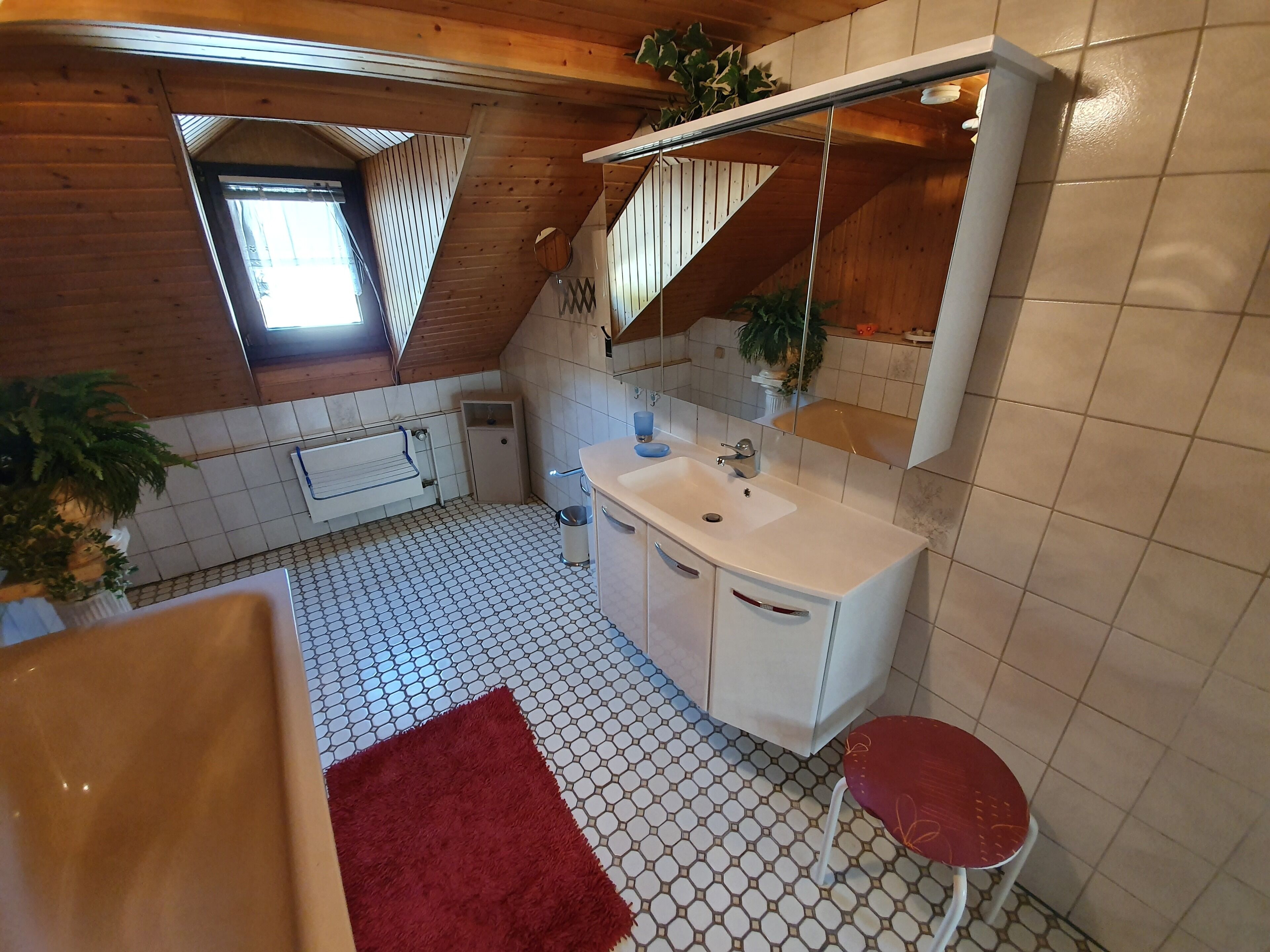 Ein kleines, gemütliches Badezimmer mit einem weißen Waschbecken, einem roten Hocker und einer Holzbalkendecke.