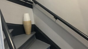 Una escalera con barandas negras y un jarrón blanco en la plataforma.
