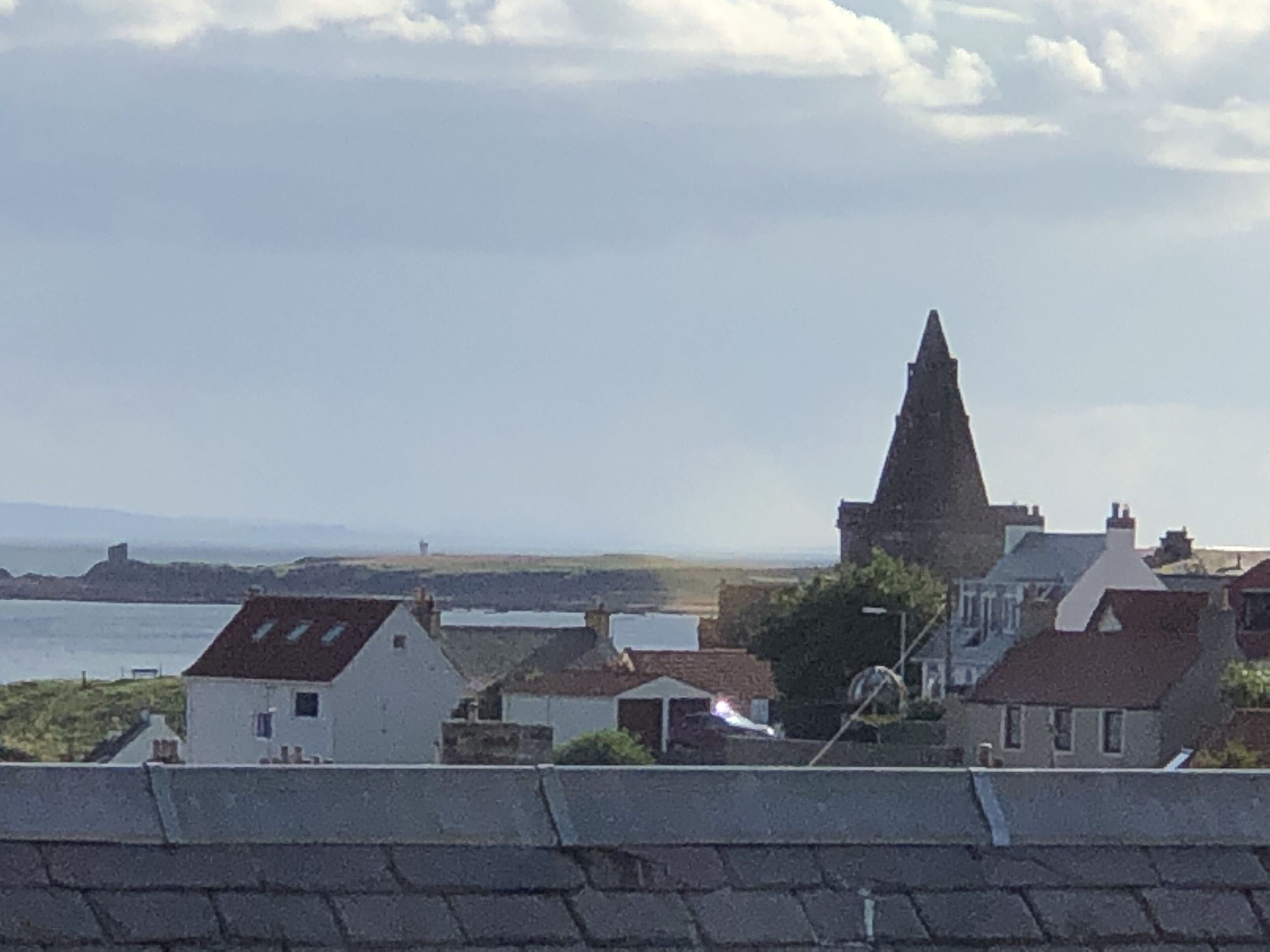 A coastal town with a prominent church spire, houses with red roofs, and a view of the sea.
