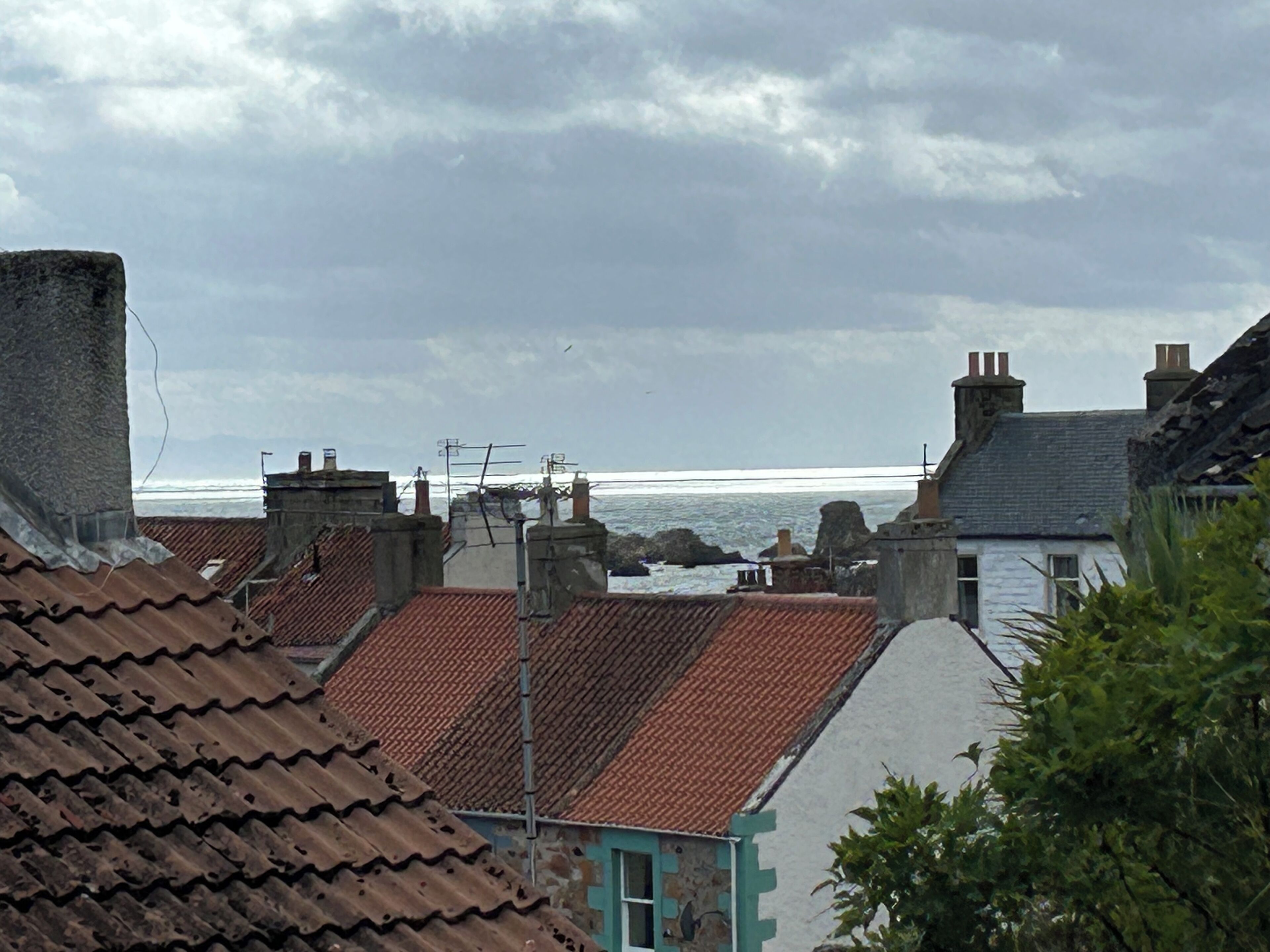 A coastal residential area with terracotta-tiled rooftops and stone chimneys.