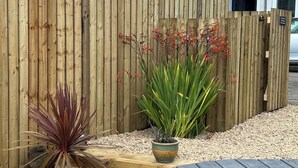 Una cerca de madera, una mesa de madera y dos plantas en macetas en un jardín.