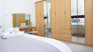 Ein Schlafzimmer mit einem Bett, einem Holzschrank, einem Spiegel und einem Schreibtisch mit Stuhl.