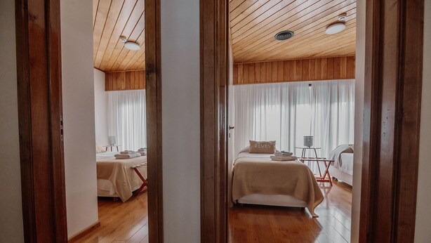 A hotel room with wooden flooring, a bed with a beige bedspread, a bedside table with a lamp, and a window with sheer curtains. - Large close to Downtown appartment (Ushuaia)