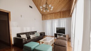 A living room with a sofa, ottomans, a coffee table, a TV, and a chandelier. - Large close to Downtown appartment (Ushuaia)