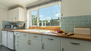 Eine Küche mit weißen Schränken, einer Mikrowelle, einer Brotdose und einem Fenster mit Blick nach draußen.