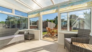Eine sonnendurchflutete Terrasse mit Korbmöbeln, großen Fenstern und Blick auf den Garten.