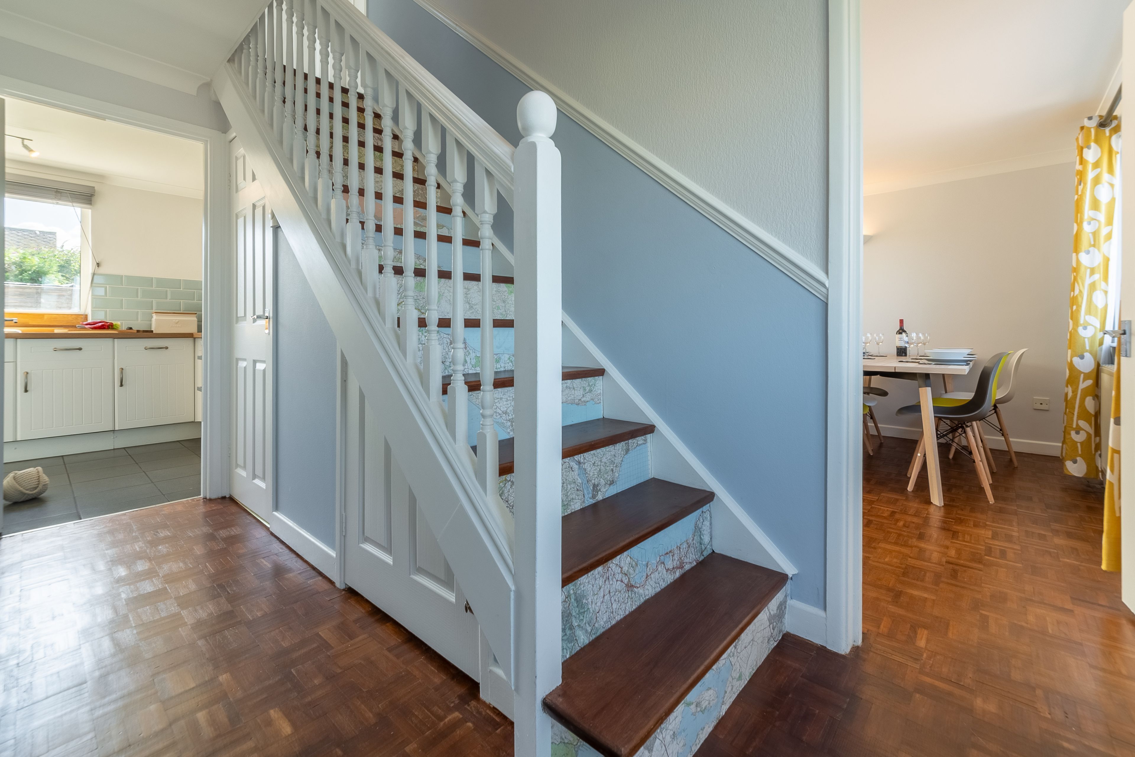 A staircase with white balusters and wooden steps, leading to a dining area with a table and chairs.