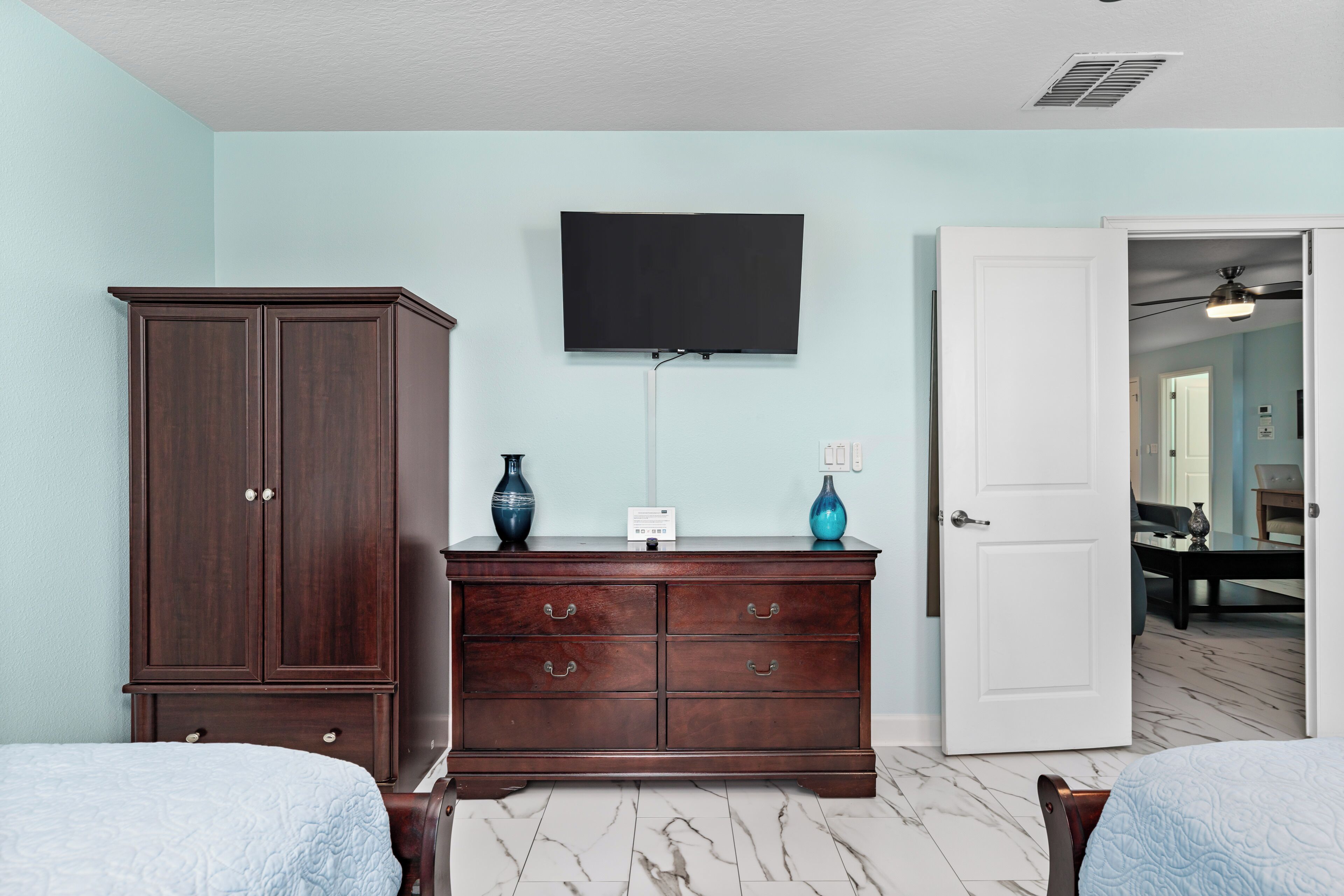 Un dormitorio con un gran aparador de madera, un televisor de pantalla plana montado encima y una puerta que da al baño.