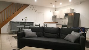 A modern living room with a black sofa, a wooden coffee table, and a kitchen in the background.