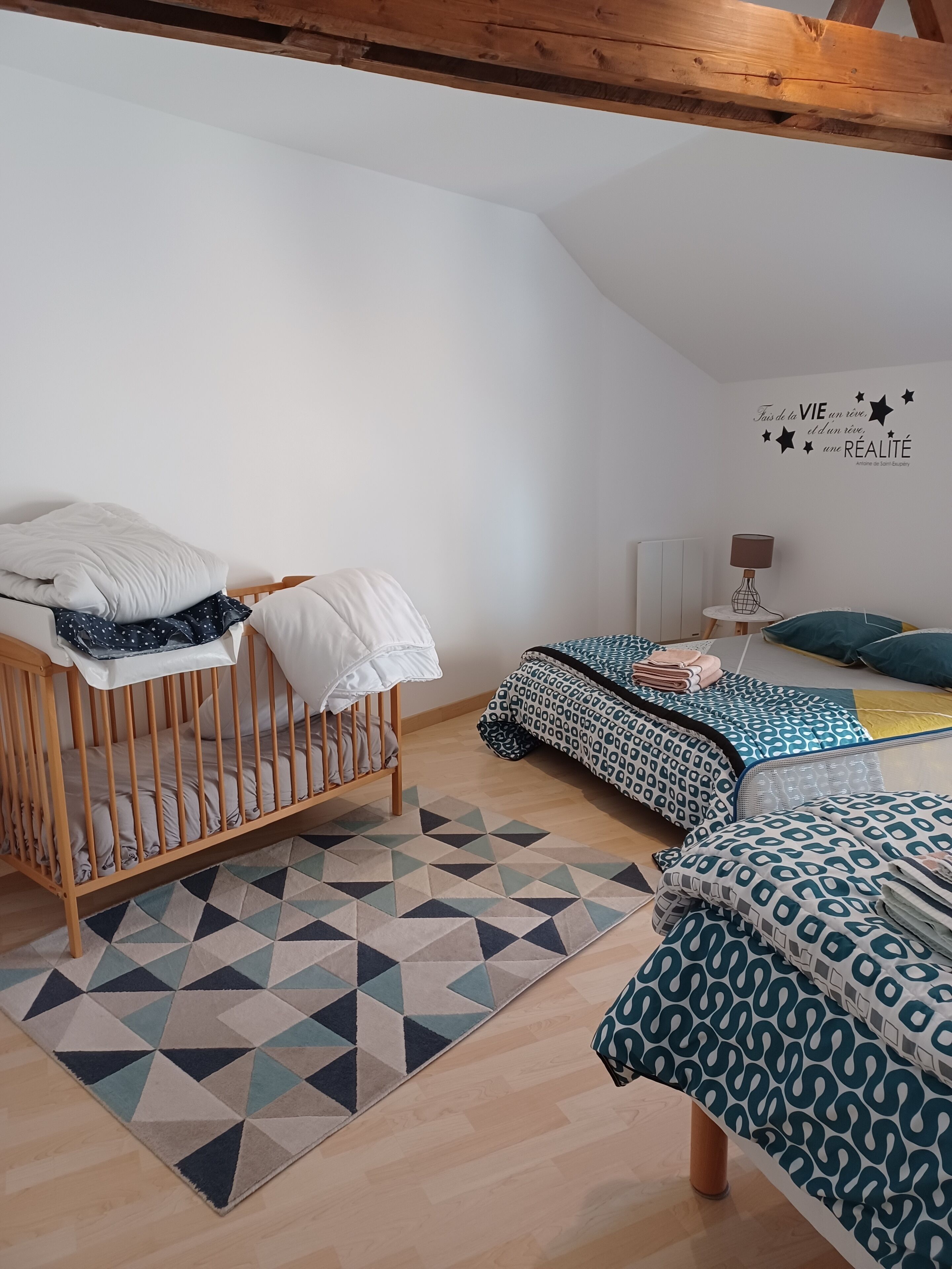 A cozy bedroom with a wooden crib, a bed with patterned bedding, a geometric rug, and a wall with a motivational quote.