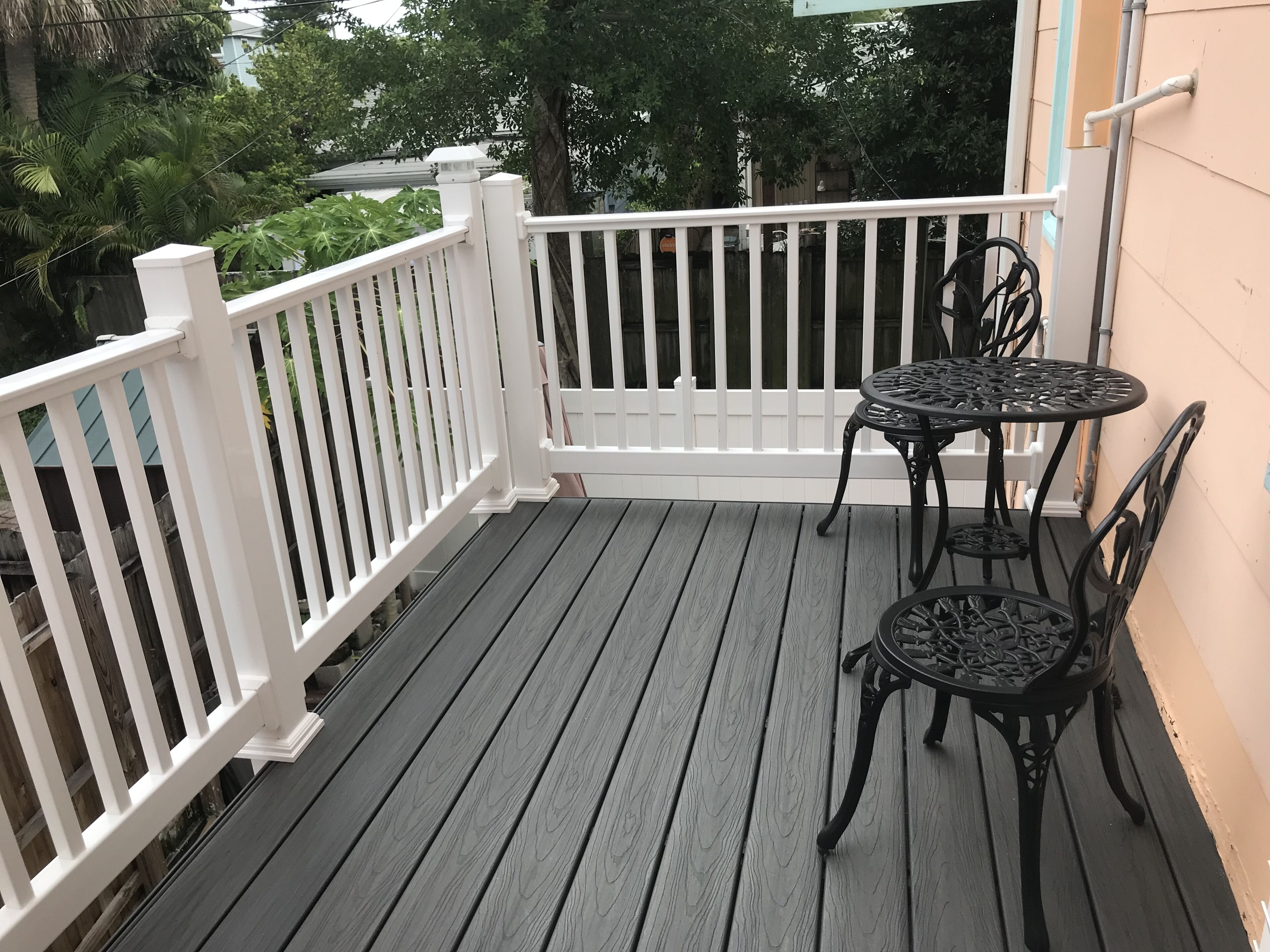 Eine Holzterrasse mit weißem Geländer, einem runden Tisch und zwei Stühlen.