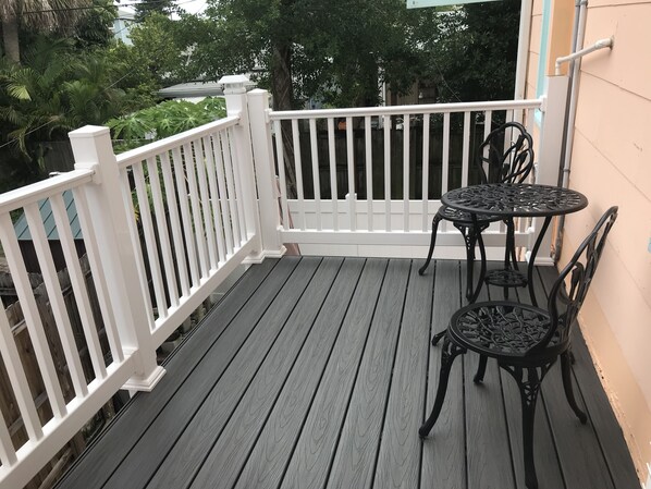 A wooden deck with a white railing, a round table, and two chairs.