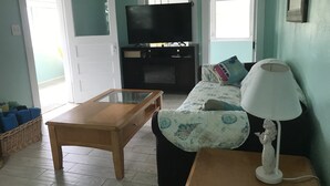 A living room with a wooden table, a sofa with patterned cushions, a white lamp, and a television on a stand. - COZY BEACH HOUSE 2 BEDROOM (Treasure island)