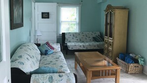 A living room with a sofa, a wooden coffee table, a cabinet, and a ceiling fan. - COZY BEACH HOUSE 2 BEDROOM (Treasure island)