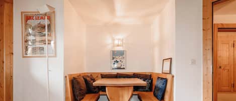 A wooden bench seating area with a table in the center, a wall-mounted light fixture, and a framed poster on the wall.
