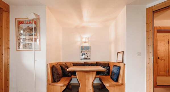 A wooden bench seating area with a table in the center, a wall-mounted light fixture, and a framed poster on the wall.