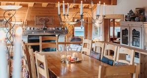 A wooden dining table with chairs, candles, and a chandelier in a room with wooden walls and cabinets.