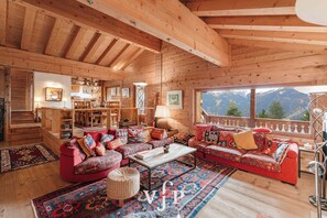 A cozy log cabin interior with a dining area, a sofa set, and a view of mountains.