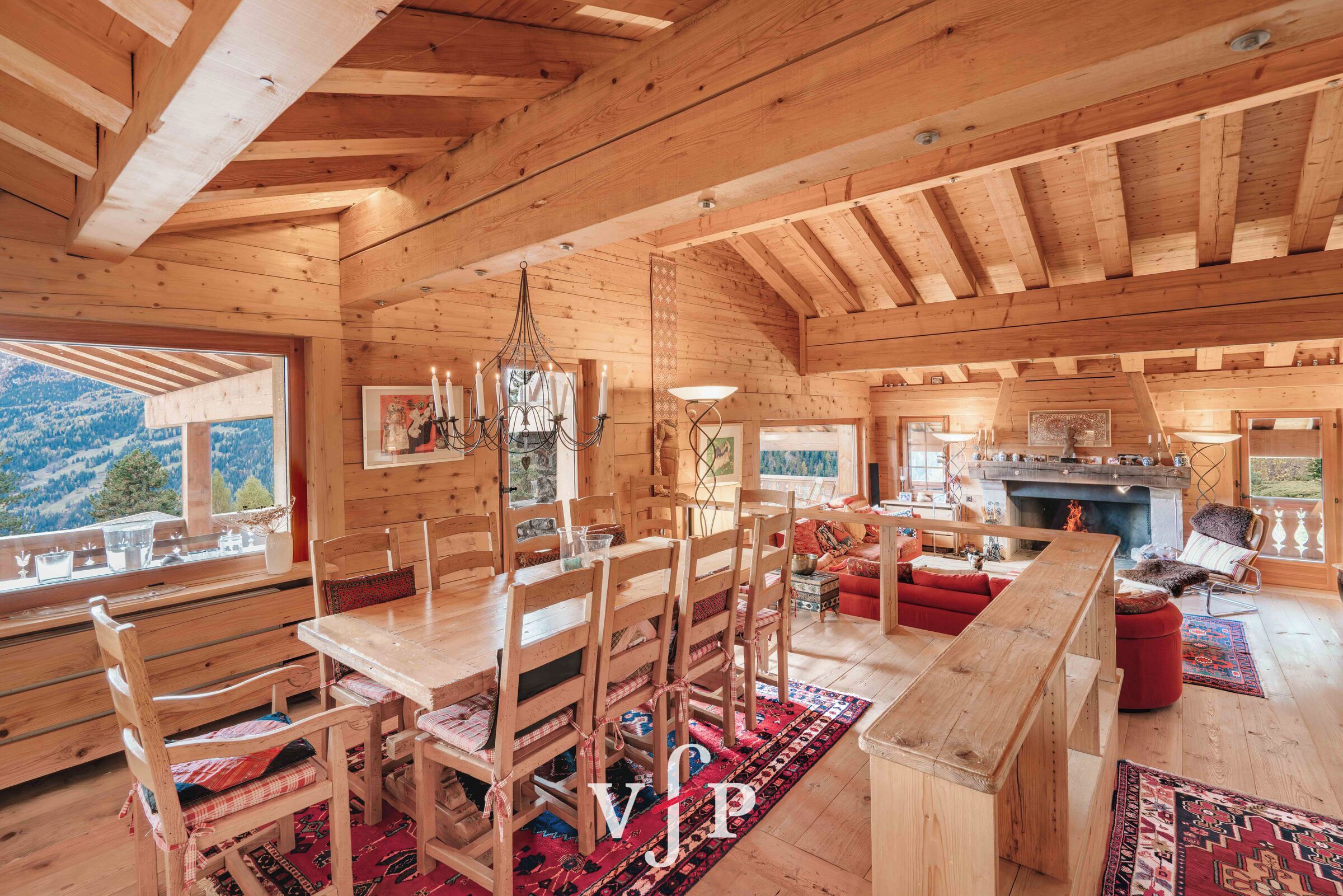 A wooden cabin interior with a dining area, a fireplace, and a view of the mountains.