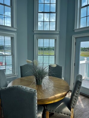 A dining area with a round wooden table, grey upholstered chairs, and a potted plant. - Star of the Sea dolphin watch (North Myrtle Beach)