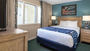 A hotel room with a bed, two bedside tables, a desk, a window with curtains, and a painting on the wall. - Two Bedroom Ocean View Luxury, Myrtle Beach 1751742 (North Myrtle Beach)