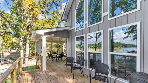 A covered deck with outdoor furniture, large windows, and a view of a lake.