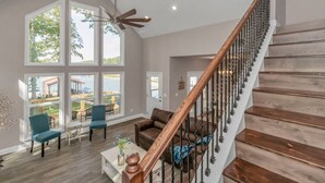 A spacious living room with a wooden staircase, large windows, and a view of an outdoor deck.
