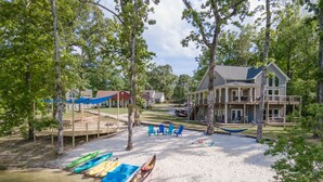 A lakeside property with a house, dock, kayaks, and outdoor seating area.