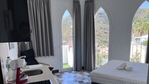 A hotel room with a bed, a sink, a chair, and a view of a hilly landscape through arched windows. - Studio and terrace with mountain views (Arenas De Velez)