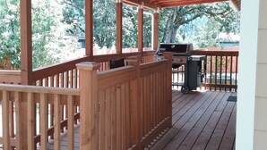 Una terraza de madera con zona cubierta, una parrilla y un bote de basura.