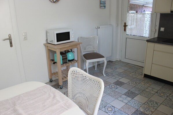 A small kitchenette with a microwave on a wooden cart, a white chair, and a tiled floor. - Holiday house in the center of Jever - In the house time-out, outside Frisian-tart (Jever)