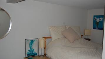 A bedroom with a bed, a bedside table with a lamp, a framed picture, and a wall-mounted mirror.