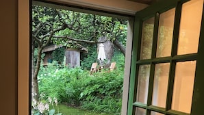 Una porta verde con un pannello di vetro, che si apre su un vialetto in pietra e un giardino con piante e una struttura in legno.
