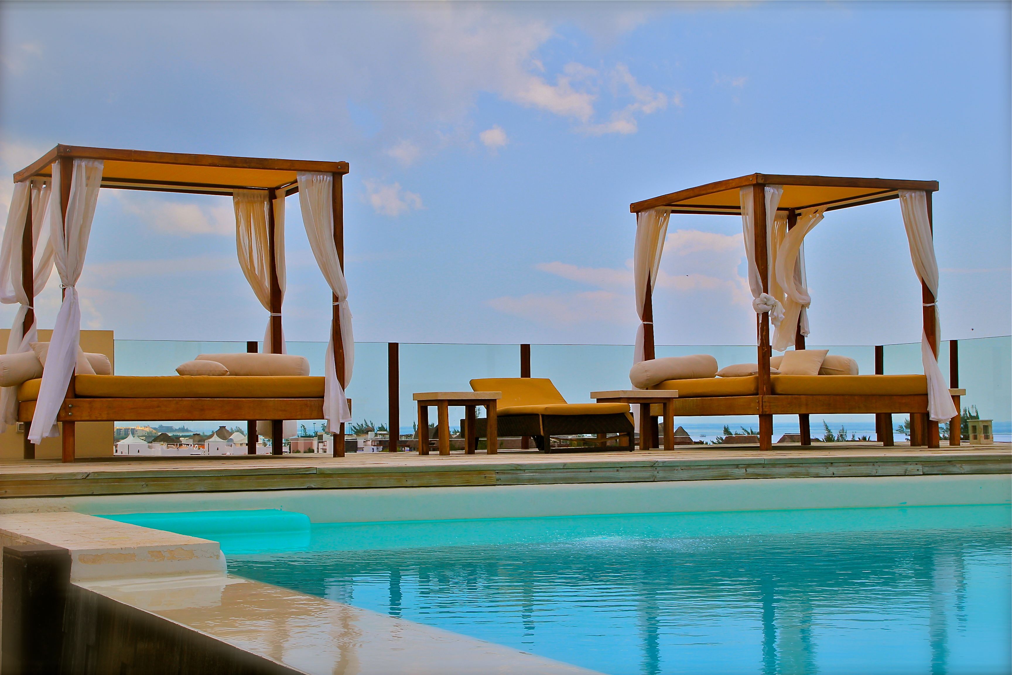A poolside area with two wooden gazebos, lounge chairs, and a clear view of the ocean.