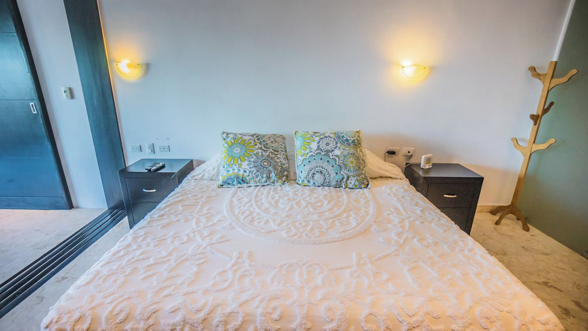 Een slaapkamer met een groot bed, twee nachtkastjes, een houten kapstok en twee wandlampen.