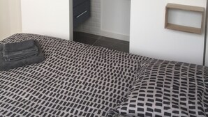 Makuuhuone, jossa on sänky, lipasto, lamppu ja seinään kiinnitetty valaisin.